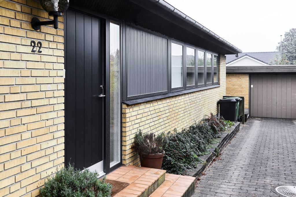 Facade af gult murstenshus med sorte hoveddør og vinduer fra VELFAC.