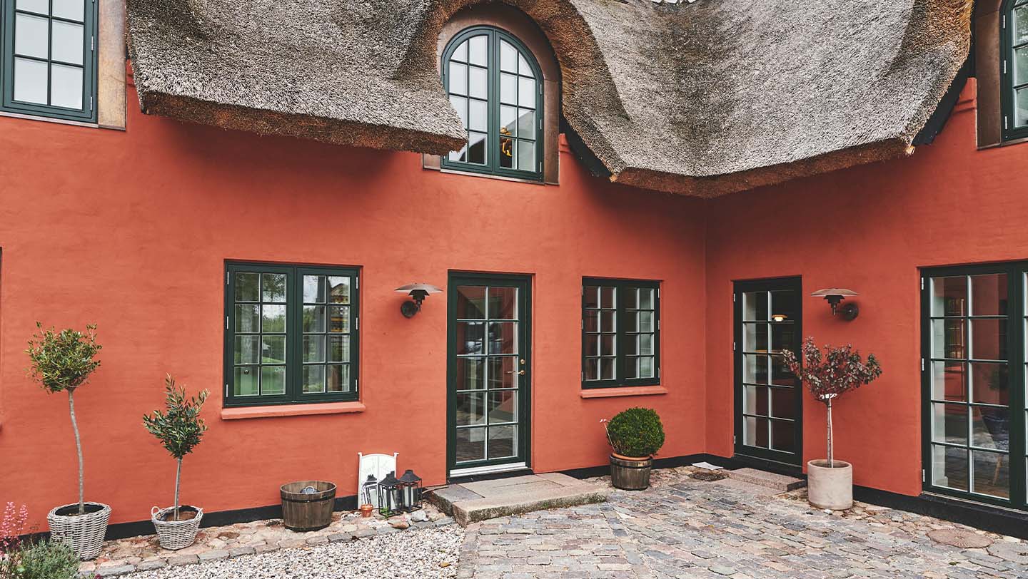 Rødt strå tag hus med grønne sprossede vinduer