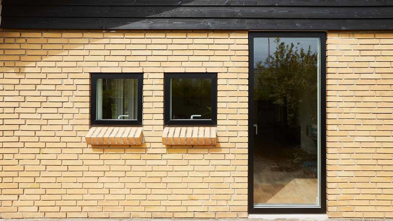 Gult murstenshus med sorte VELFAC vinduer og terrassedør.